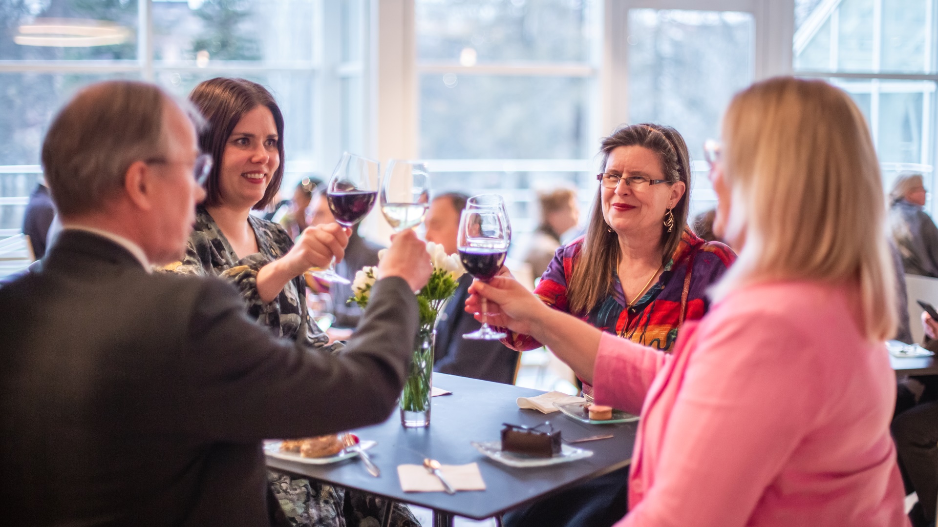 Four people sit at a table with interval catering and raise a toast.
